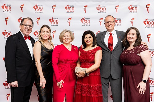 Group of six guests in front of American Heart Association 100 years of bold hearts banner